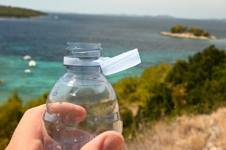A plastic bottle with a tethered cap and the sea in the background.