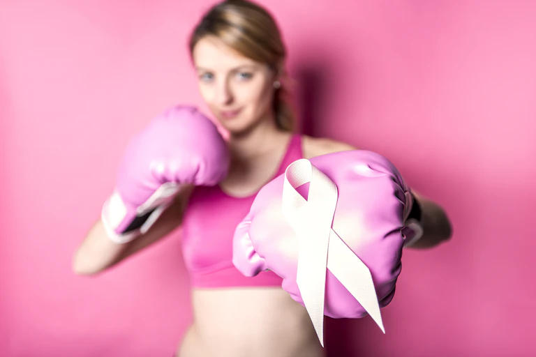 Une femme en tenue de sport porte des gants de boxe avec, sur un des gants, le ruban d'octobre rose.