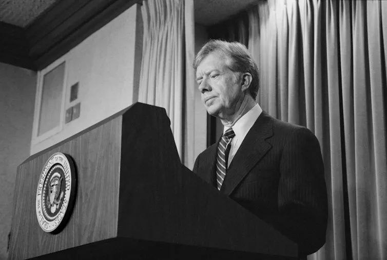 A middle aged man with a stern face stands behind a podium.