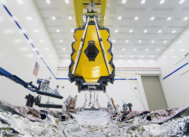 Large telescope with yellow mirrors hanging from ceiling in white room.