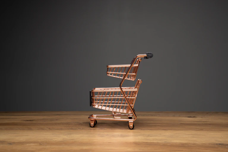 Small empty shopping cart or metal trolley in copper colour on top of wooden top and dark background