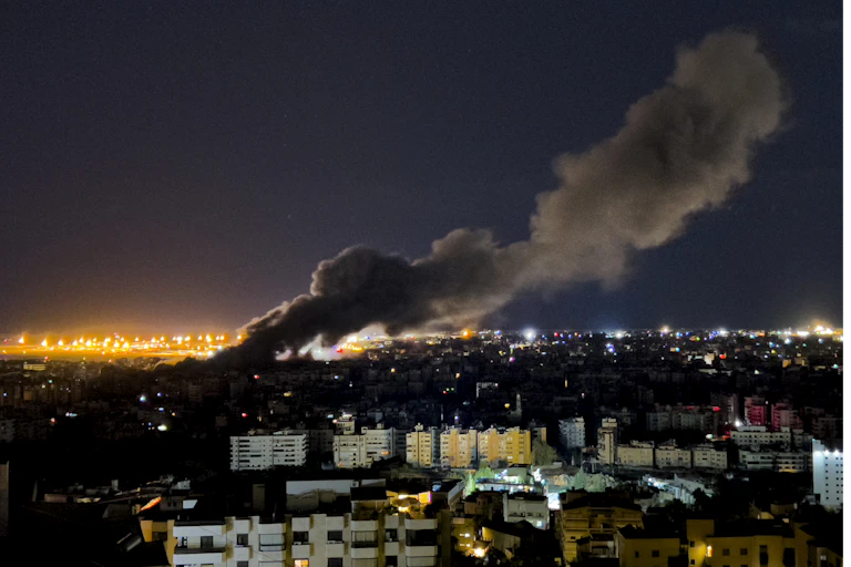 A cityscape at night with a large plume of smoke billowing up