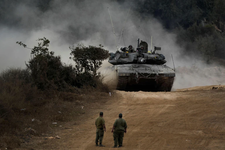 Two IDF soldiers look on as an Israeli tank manoeuvers at the Lebanese border.