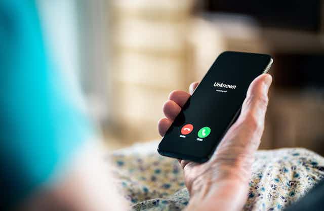 La main d'une personne âgée tient un téléphone cellulaire.