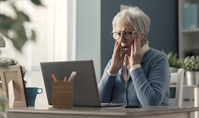 An elderly woman, bewildered in front of her computer