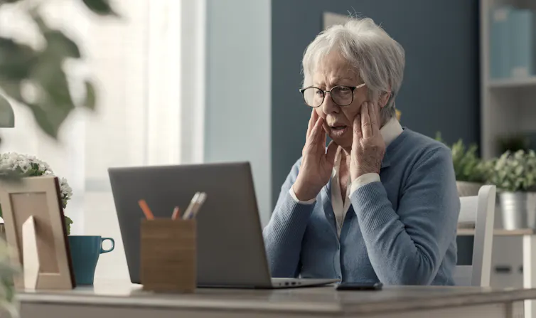 An elderly woman, bewildered in front of her computer