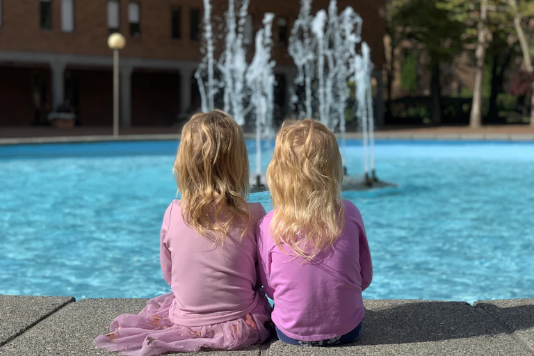 two young girls facing away from camera are looking at a fountain