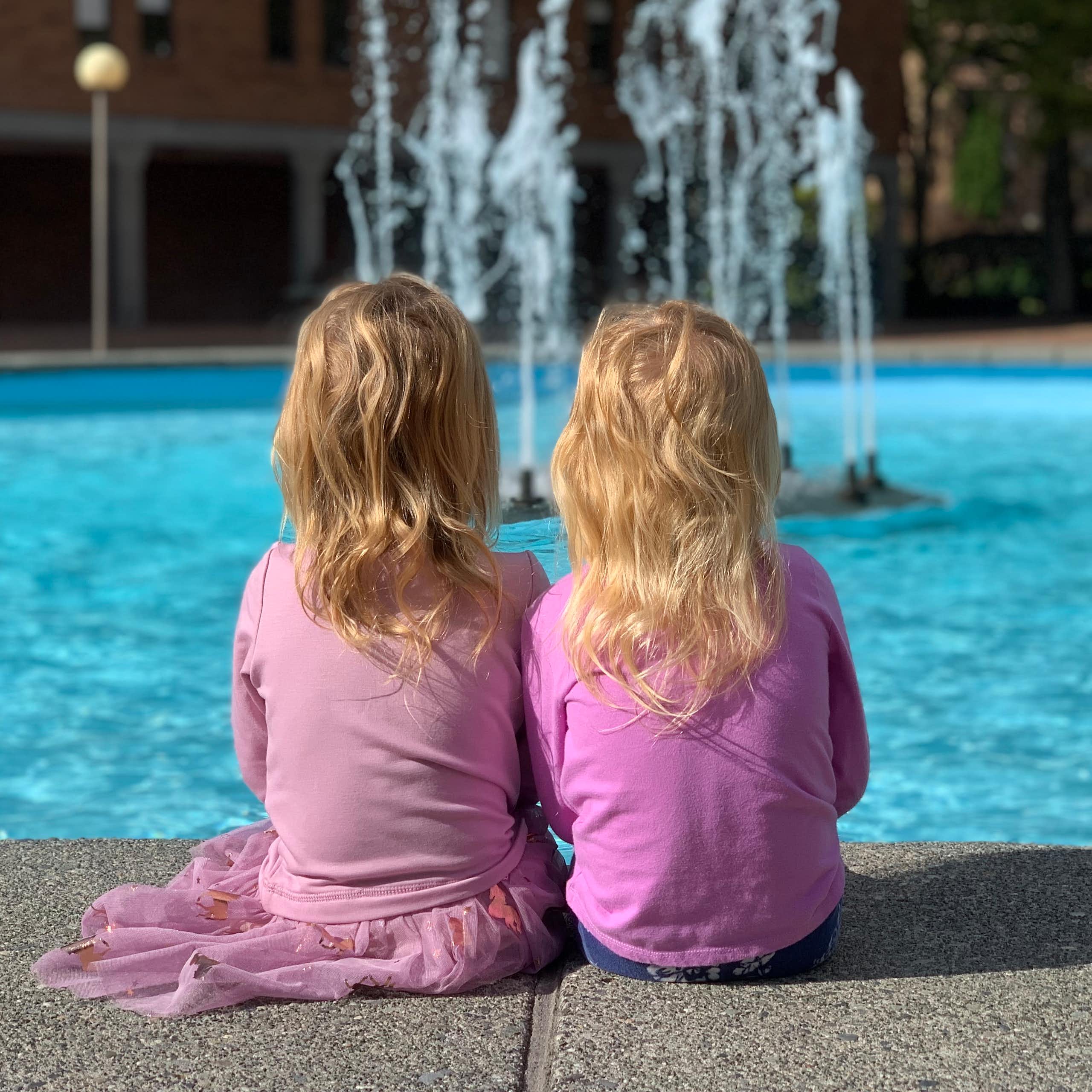 two young girls facing away from camera are looking at a fountain