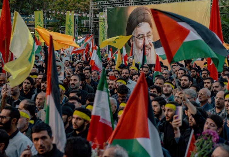 A large group of men hold red, white, black and green flags and stand together in the street.