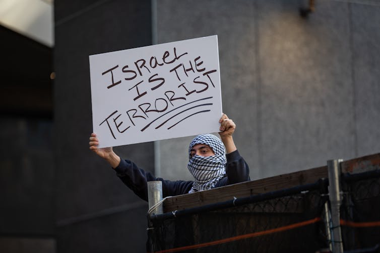 A person wearing a keffiyeh holds a sign that states