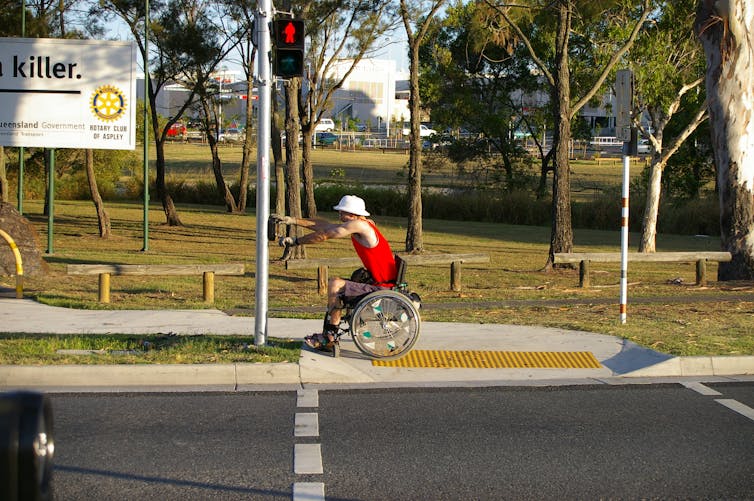 A man in a wheelchair activates crossing lights at a kerb cut