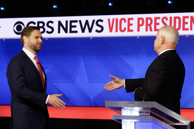 Two men in dark suits shaking hands on a stage.