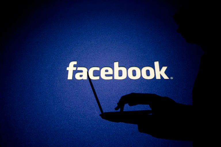 A person in shadow works on a computer in front of Facebook sign.