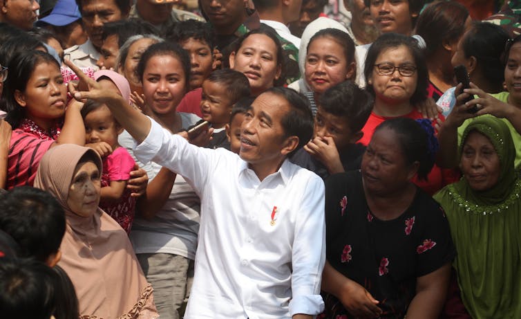 Indonesian outgoing president, Joko Widodo, stands and speaks among a crowd of women.