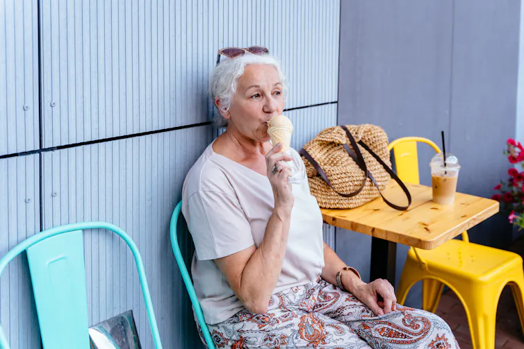 An older woman with white hair eats an ice cream.