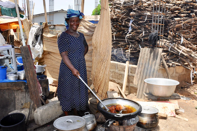 A woman stands outside cooking over a fire