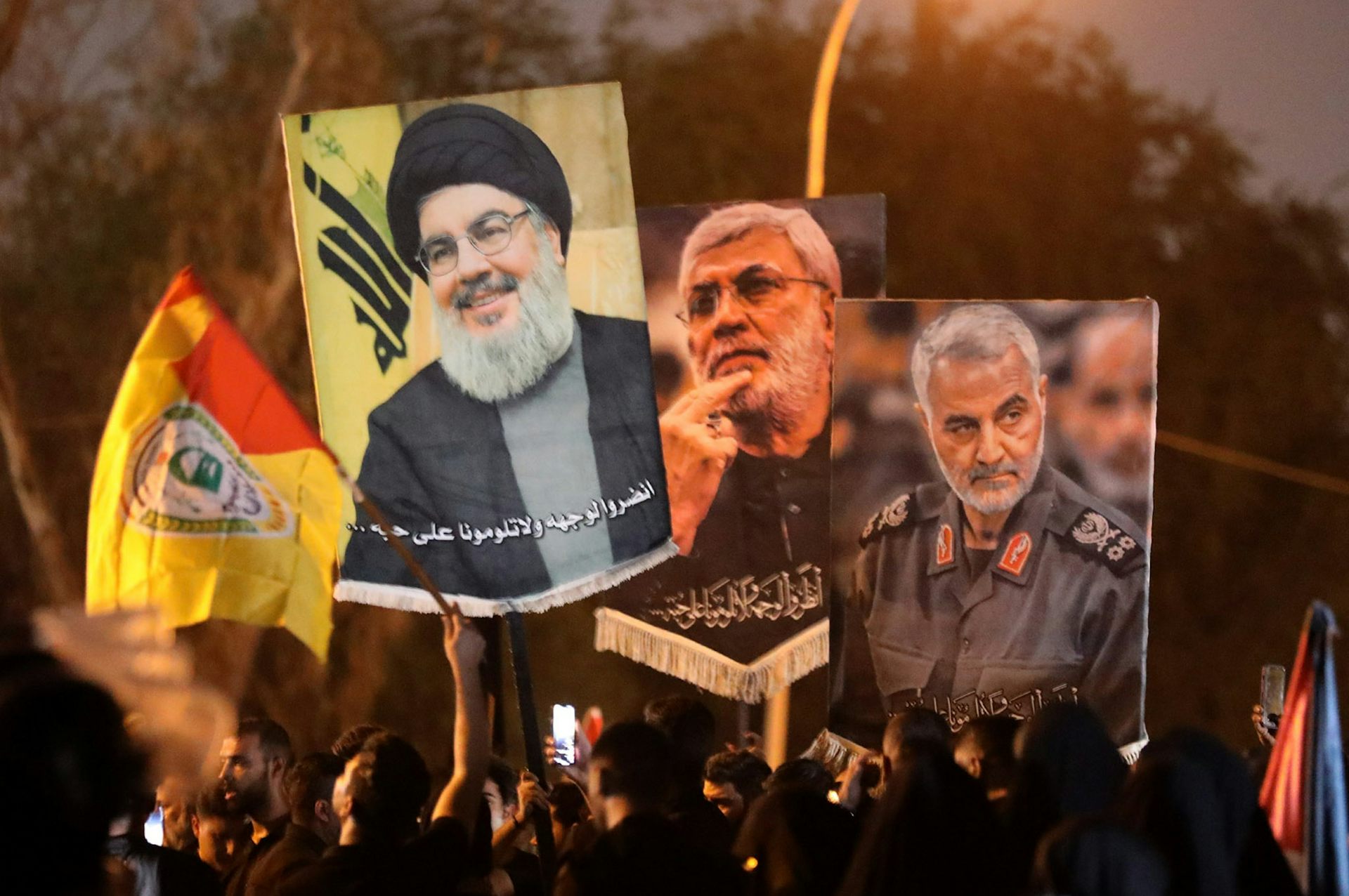 Protesters carry banners with pictures of Qassem Soleimani, Abu Mahdi al-Muhandis and Hassan Nasrallah.