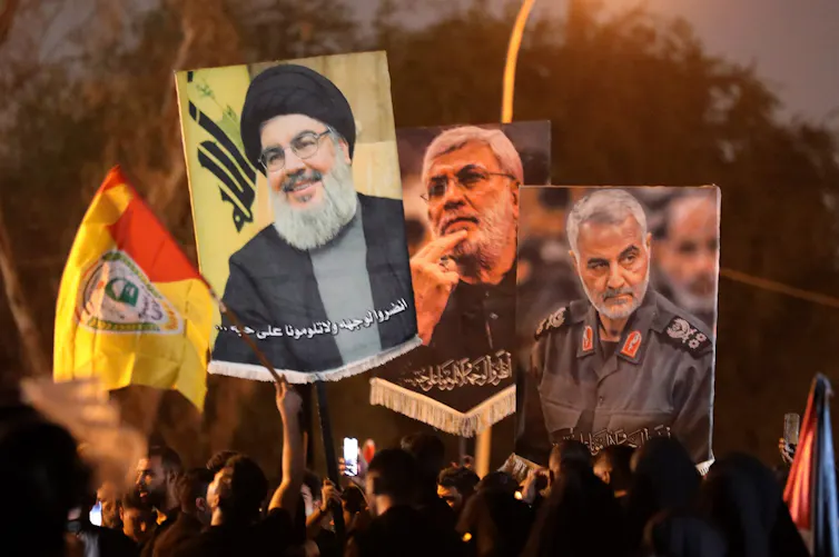 Protesters carry banners with pictures of Qassem Soleimani, Abu Mahdi al-Muhandis and Hassan Nasrallah.