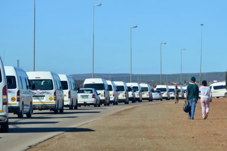 Scores of minibus taxis pass pedestrians on a street