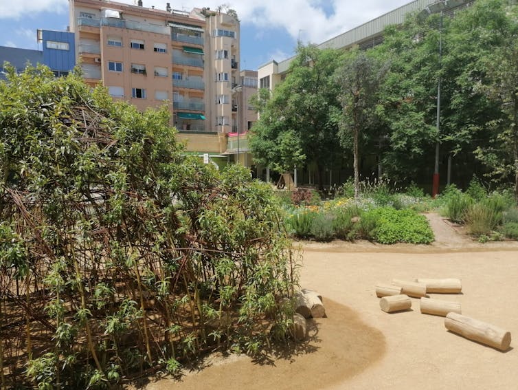 Patio escolar con elementos naturales como árboles, arbustos y troncos.