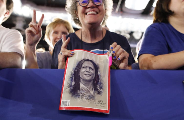 A woman holds up a black and white magazine cover that shows a drawing of a woman.