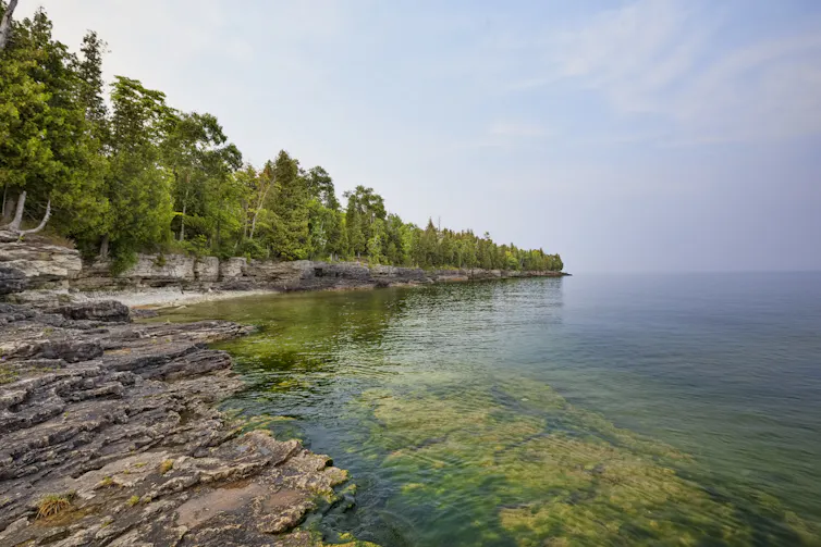 Scenic view of limestone cliffs with trees alongside calm body of water