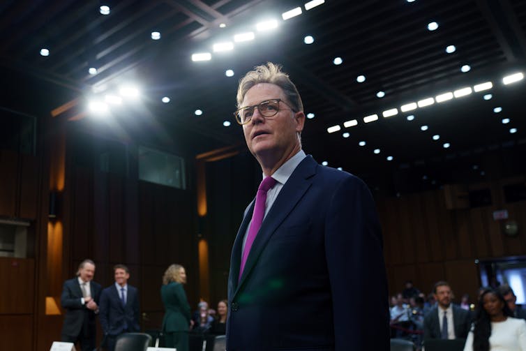 Man in suit under bright lights in senate building.