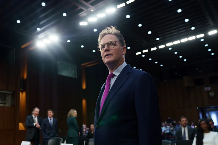 Man in suit under bright lights in senate building.