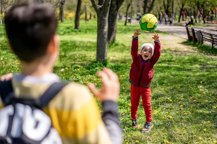 A child about to throw a ball to someone with their back to the camera