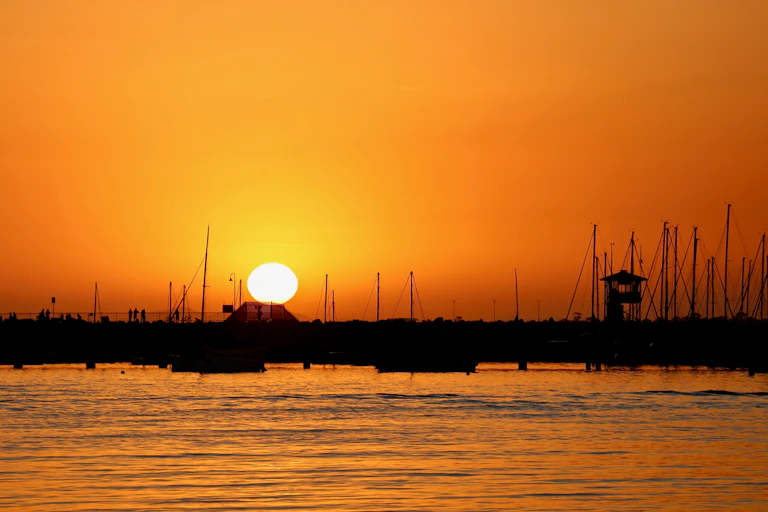 Setting sun in bright orange sky with silhouetted pier.
