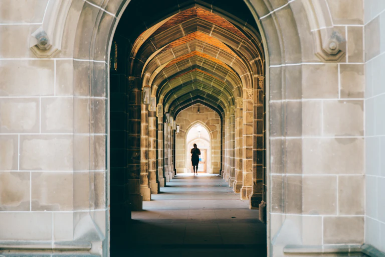 A sandstone arched walkway. A figure in shadow walks in the distance.