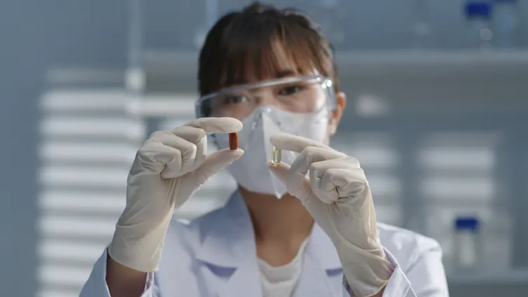 A woman in a lab coat holds two pills