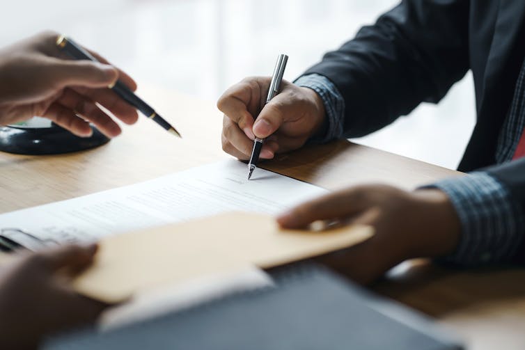 Closeup hands passing formal documents across a table