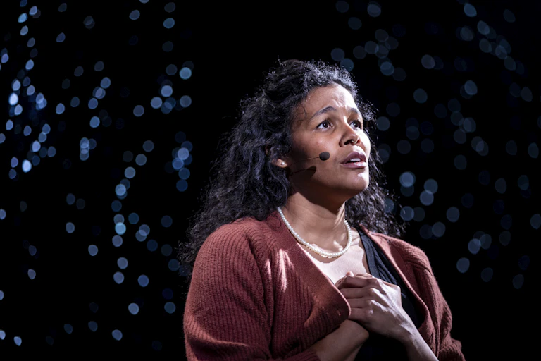 A woman sings a hearfelt song under an onstage spotlight.