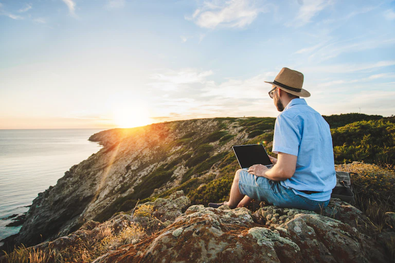 man on a clifftop with a laptop as the sun sets