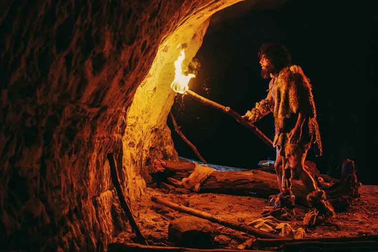 Man in cave holding fire up to paintings