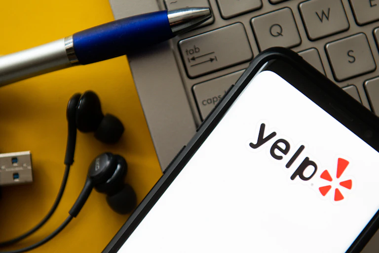 A smartphone on a laptop keyboard, with the screen of the smartphone featuring the text 'yelp.'