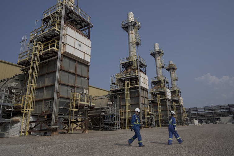 Two people walk past an industrial plant.