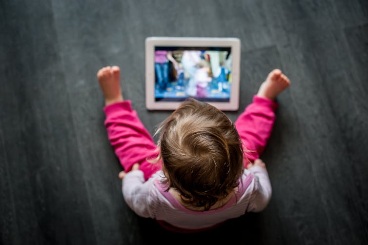 A small child wearing pink sitting on the floor looking at a tablet