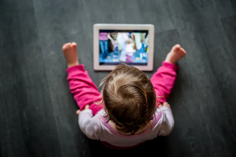 A small child wearing pink sitting on the floor looking at a tablet