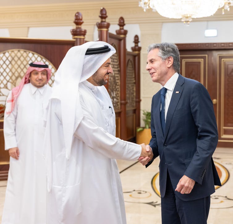 A man in flowing robes shakes hands with a man in a business suit.