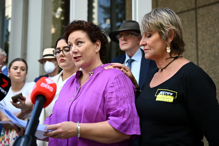 A woman in purple addresses the media, flanked by supporters
