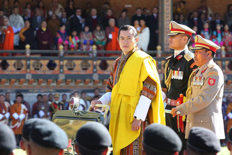 King wearing yellow robes flanked by men in military uniform