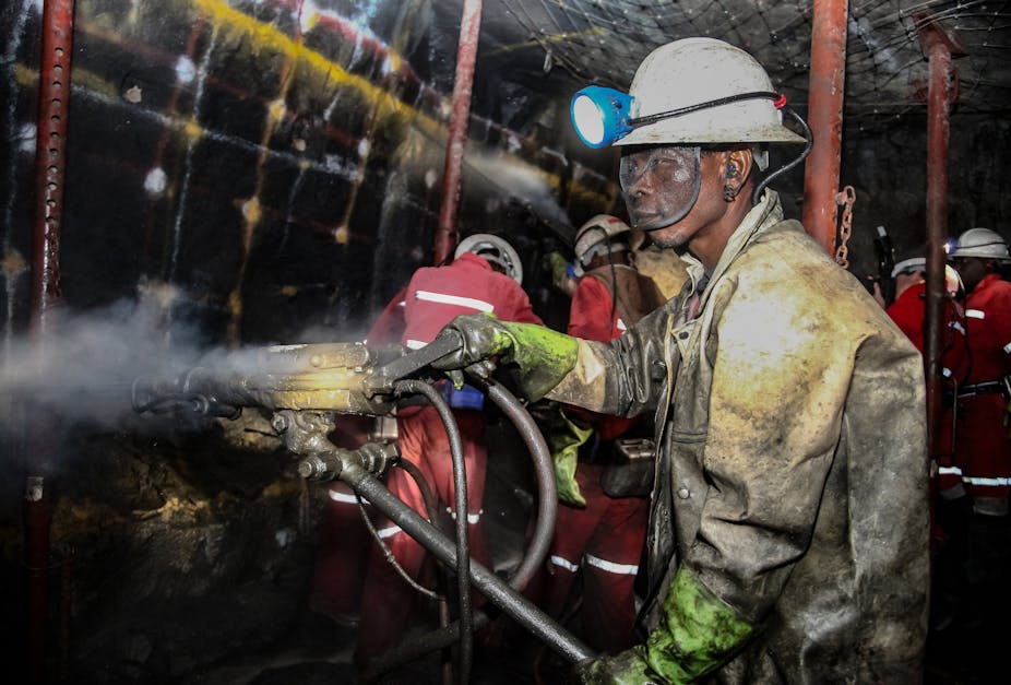 A man in a hard hat and a heavy uniform, his eyes protected by safety goggles, works underground in a mine