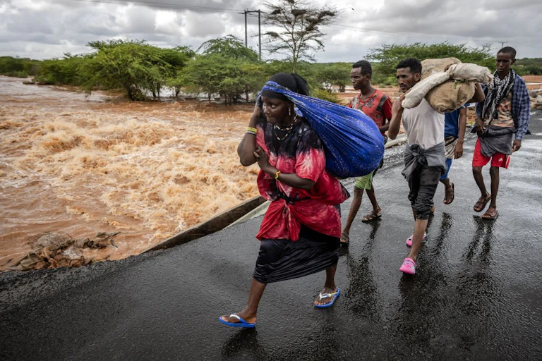 People on foot carry bundles on a wet bridge over a torrential river