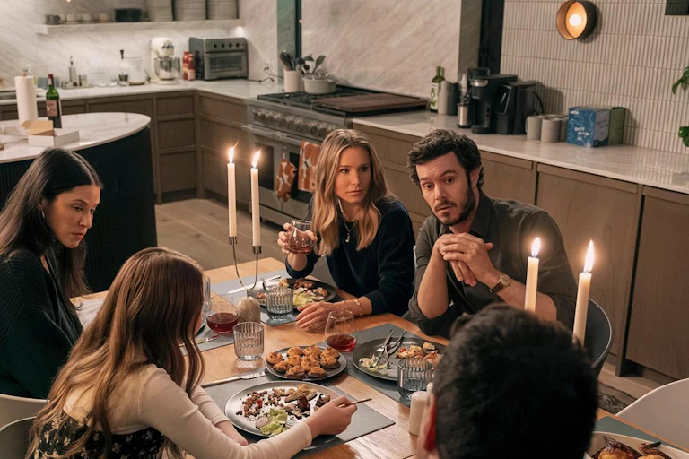 Varias personas se reúnen alrededor de una mesa ante comida y velas encendidas.