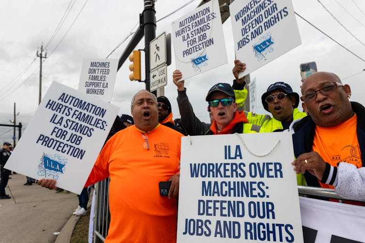 Workers shout while holding sighs saying 'ILA: Workers over machines, defend our jobs and rights.'