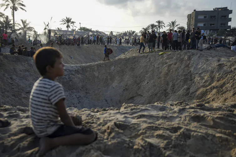 A boy sits next to a crater.