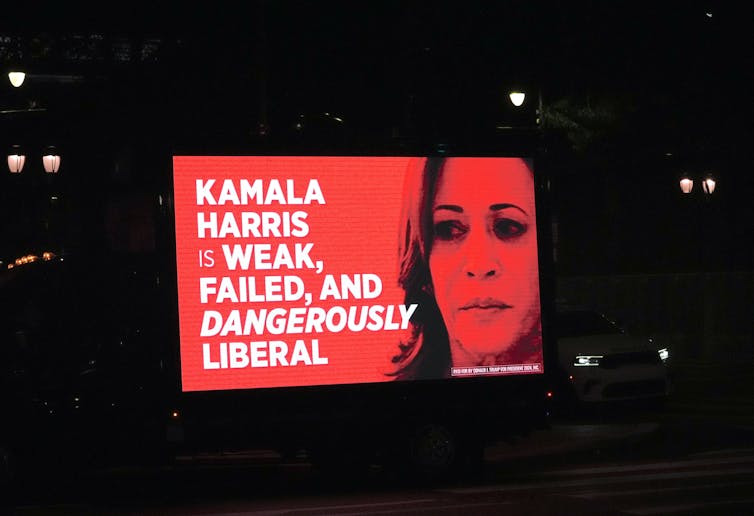 A red billboard showing a woman's face and the words 'Kamala Harris is weak, failed, and dangerously liberal.