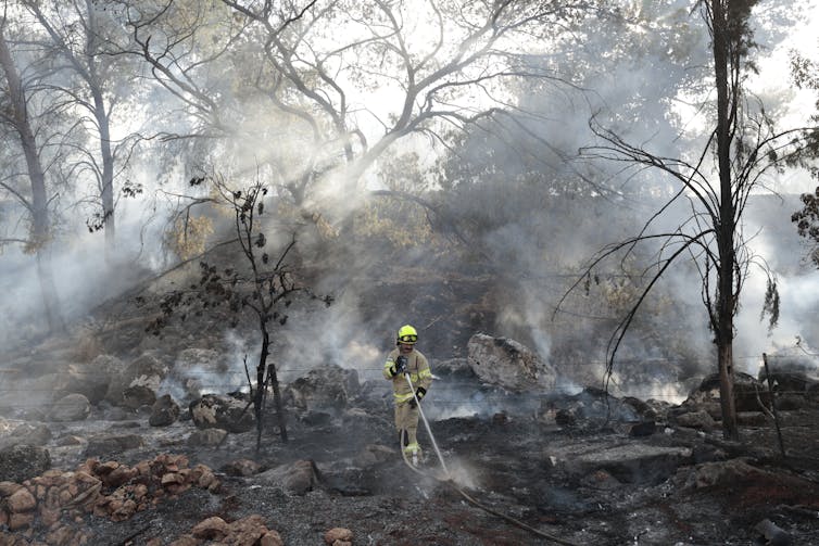 Smoke billows around a solitary firefighter who is dousing the ground with a hgose.